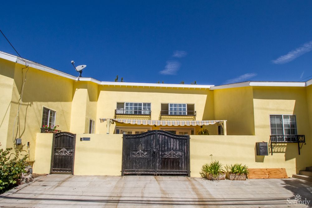 A bright yellow residential house with a gated entrance under a clear blue sky.