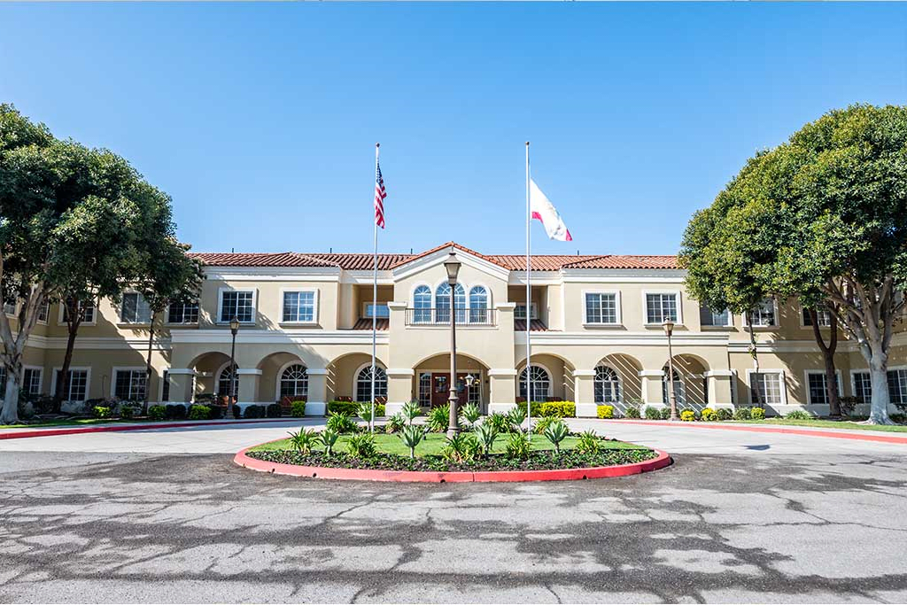 A symmetrical building with flags and a circular driveway lined with trees.