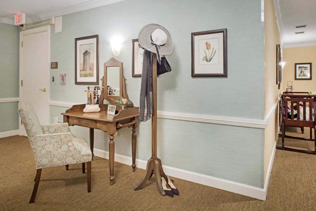 A vintage-style room with a wooden vanity desk, mirror, and coat rack against a pastel-colored wall adorned with framed art.