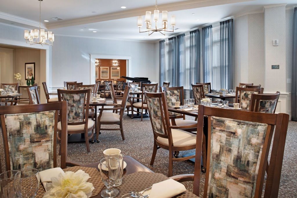 Elegant dining room with neatly arranged tables and chairs, featuring large windows and chandeliers.