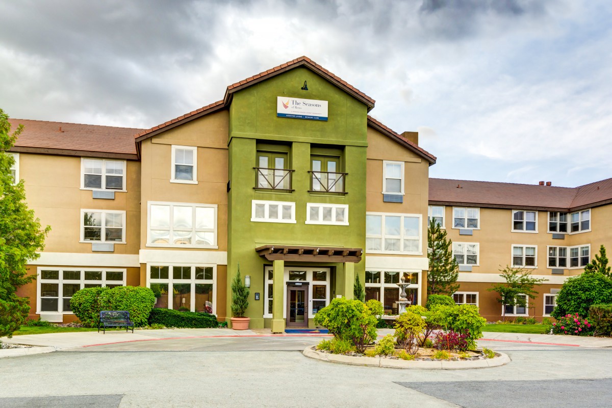 Exterior view of a hotel building with a landscaped entrance under a cloudy sky.