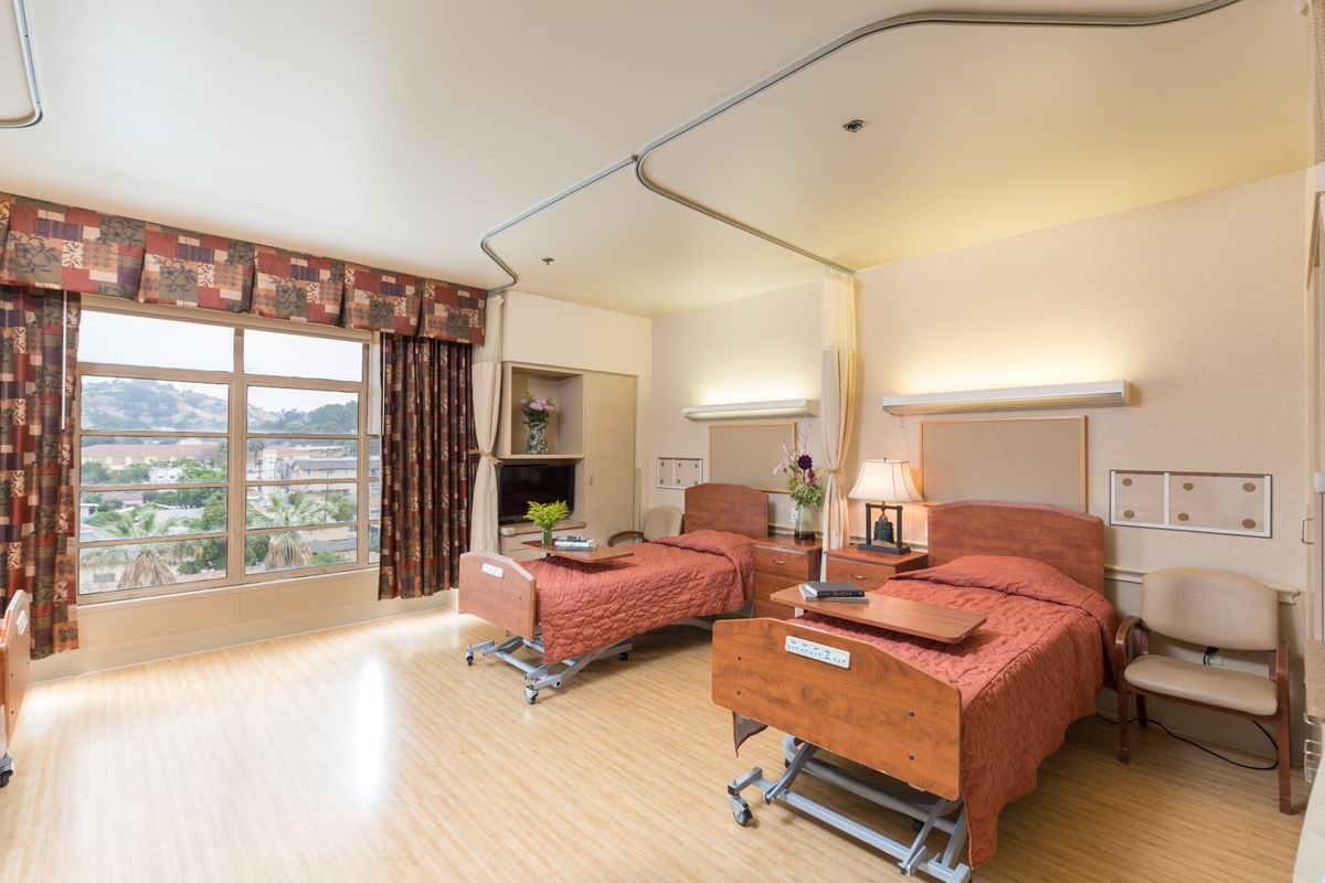 A well-lit hospital room with two patient beds and a view of the outdoors.