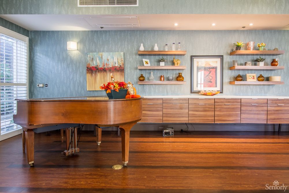 A stylish living room featuring a grand piano, wooden floors, and decorative shelves with artwork.
