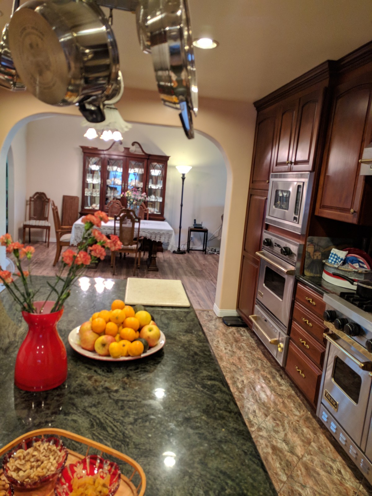A cozy kitchen with a view into a dining room, featuring a countertop with oranges in a bowl and flowers in a vase.