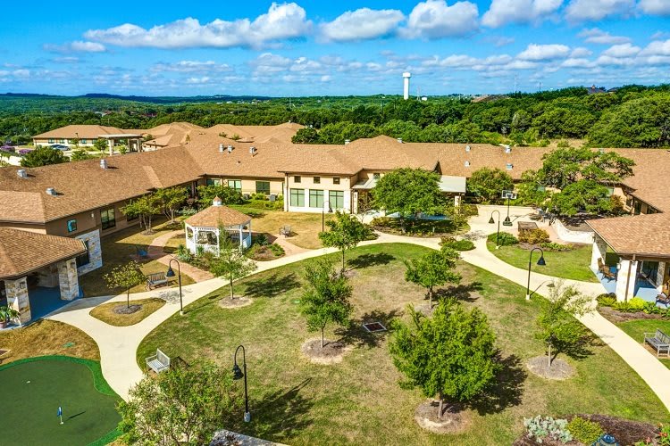 Aerial view of a building complex surrounded by landscaped gardens and pathways under a partially cloudy sky.