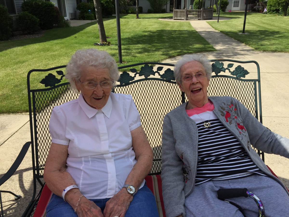 Two elderly women sitting and smiling on a bench in the park.