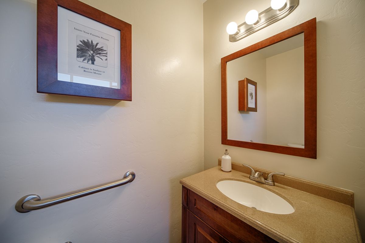 A small bathroom with a sink, mirror, wall art, and lighting above the mirror.