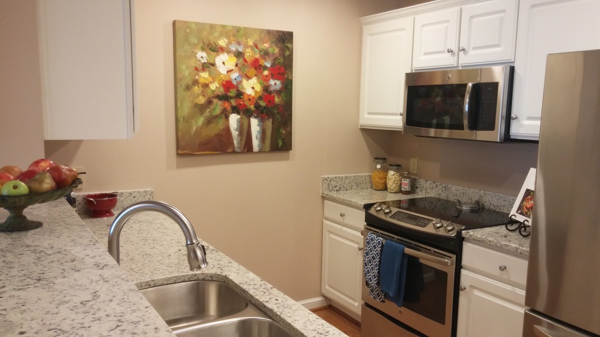 A modern kitchen with a floral painting, featuring a stove, microwave, and double sink.
