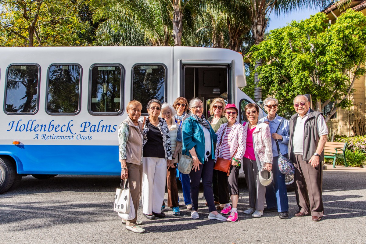 A group of seniors standing in front of a tour bus on a sunny day.
