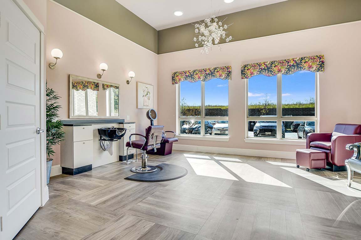 A spacious and bright hair salon interior with large windows and a styling station.