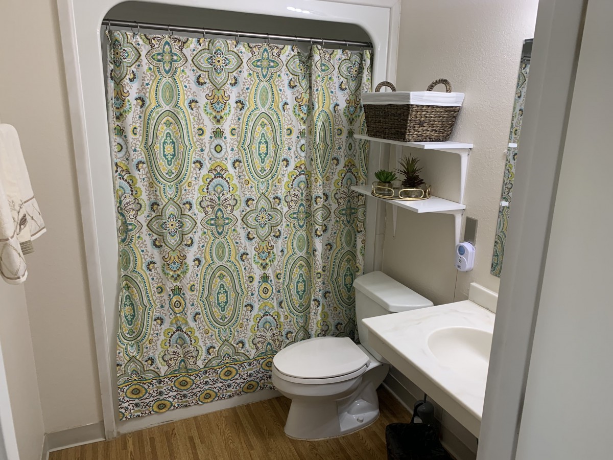A neatly organized bathroom with a patterned shower curtain and storage shelves.