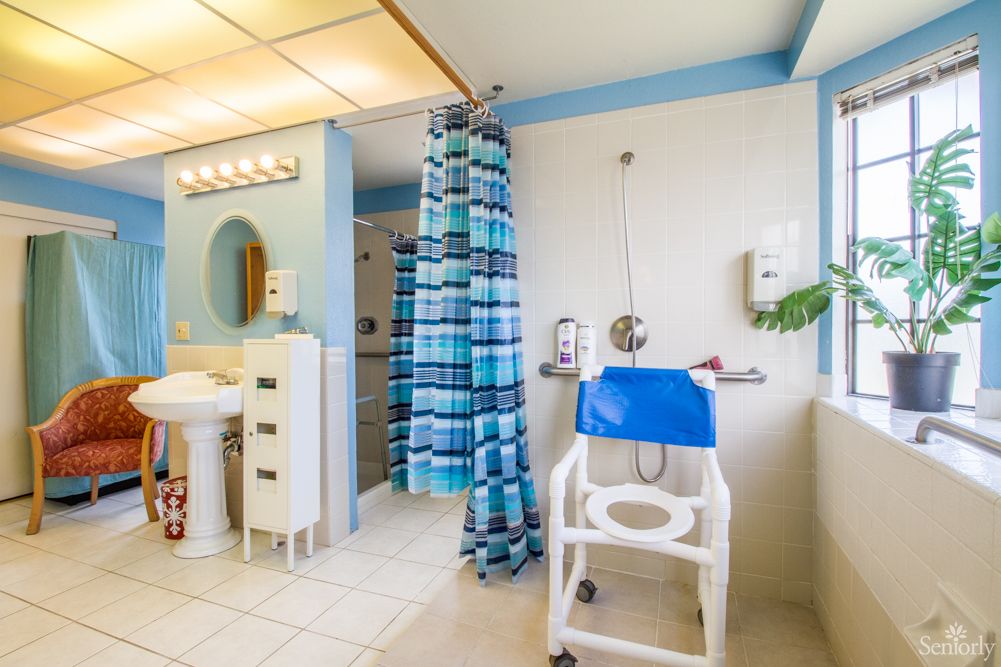 A spacious and accessible bathroom featuring a blue shower curtain, sink, and medical chair.