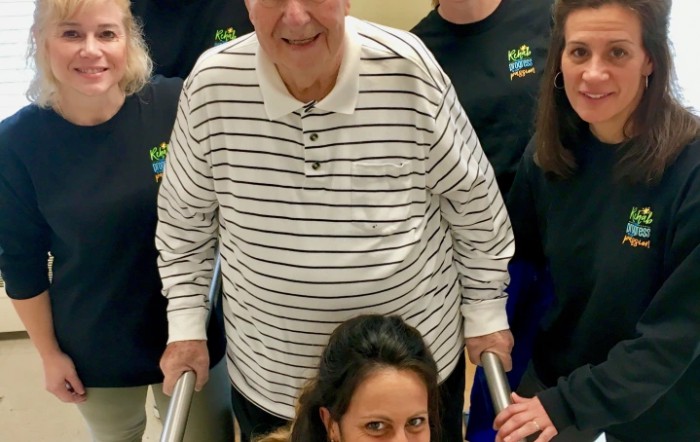 A group of people smiling indoors, with an elderly man at the center.
