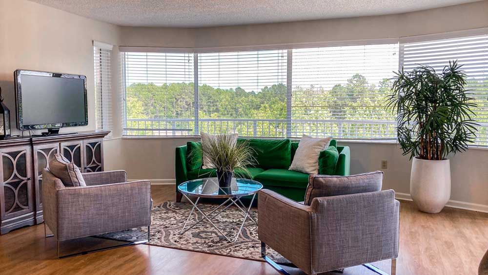 A cozy living room with a green couch, modern furniture, and large windows letting in natural light.