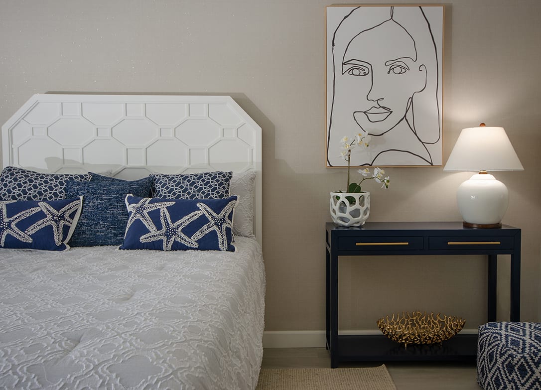 A modern bedroom with a white headboard, decorative pillows, and a minimalist artwork on the wall.
