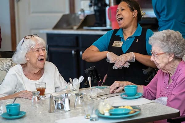 A caregiver shares a joyful moment with seniors during a meal at a community center.