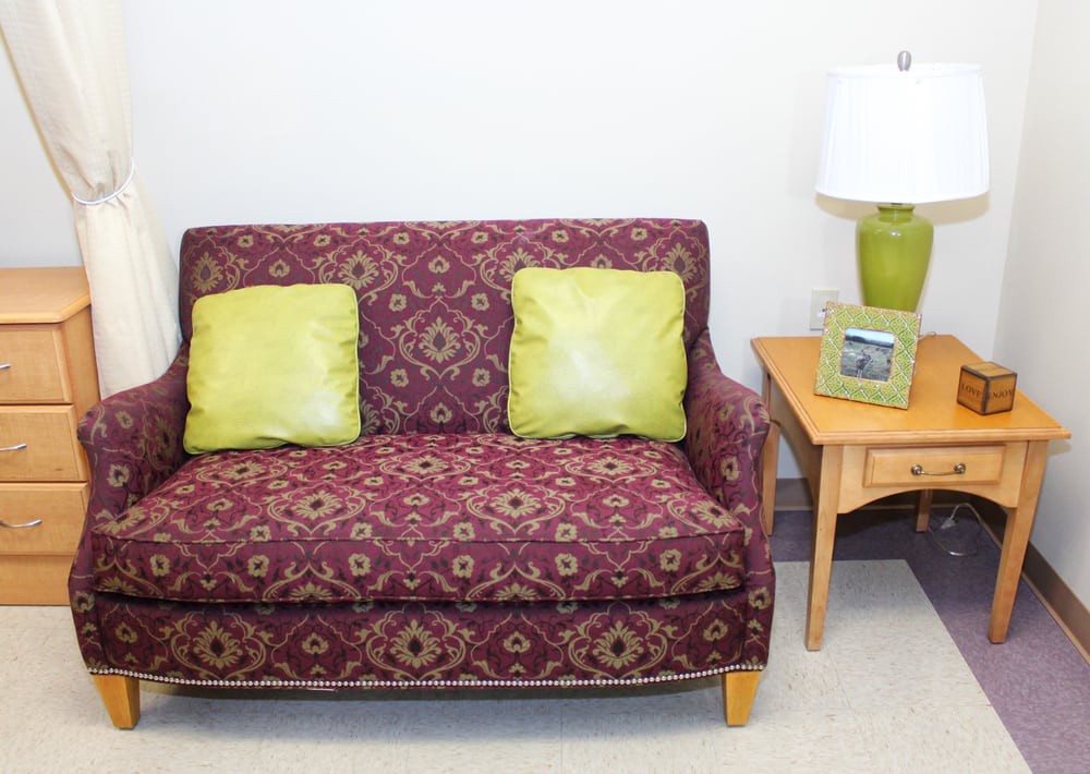 A cozy living room setup with a patterned sofa, two green pillows, and a side table with a lamp.