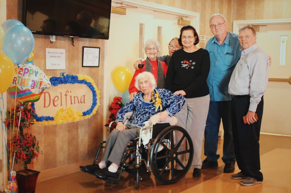 A group of people celebrating a birthday with an elderly woman in a wheelchair.