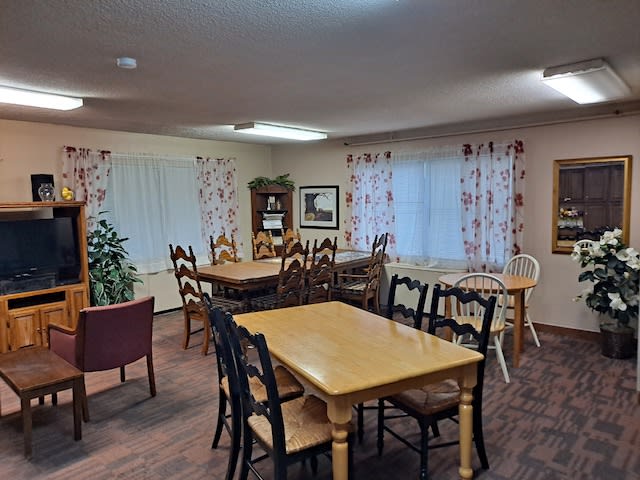 A cozy dining area with wooden tables and chairs, decorated with floral curtains and warm lighting.