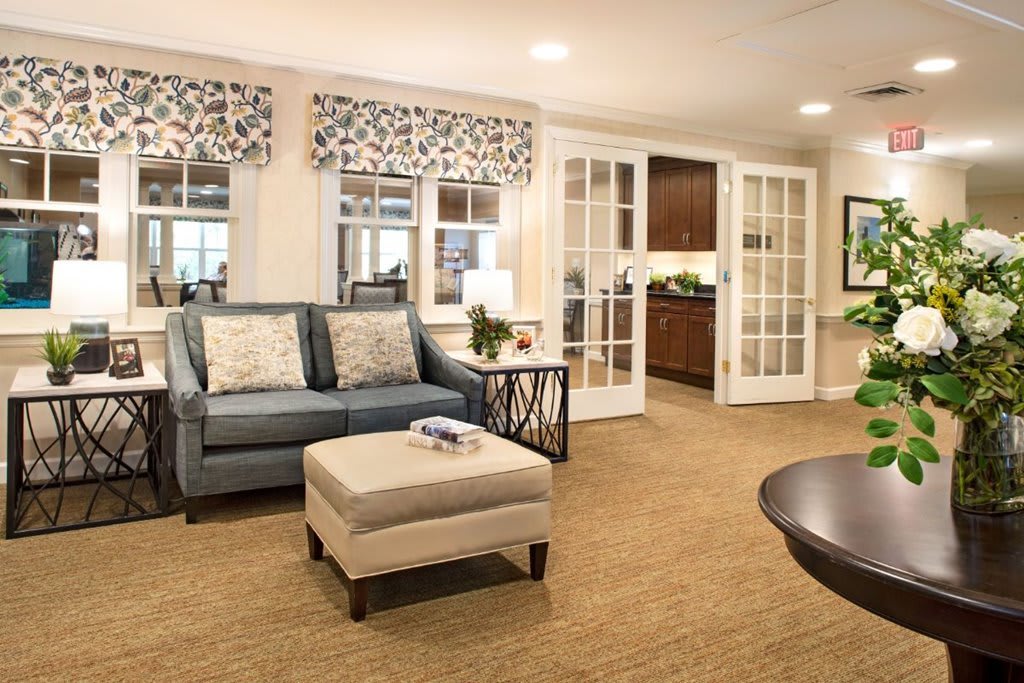 A modern and cozy living room with a sofa, ottoman, and glass doors leading to another room.
