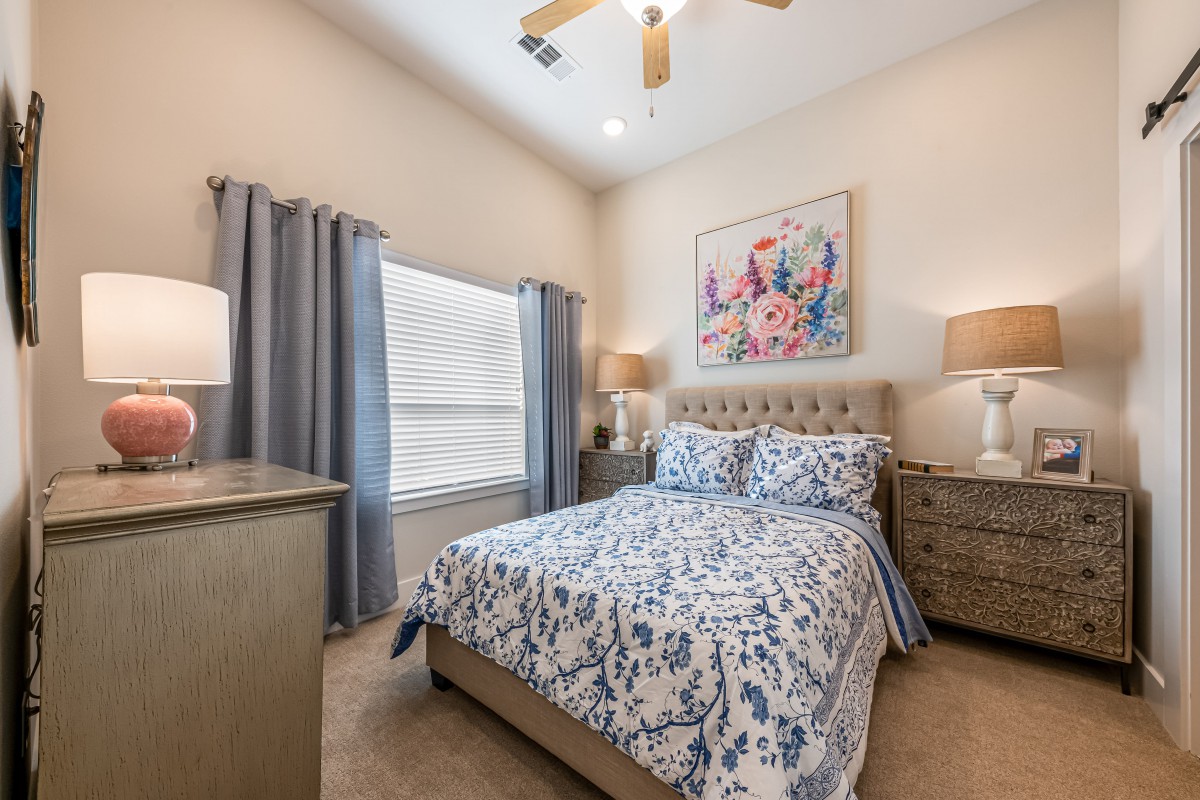 A beautifully decorated bedroom featuring a bed with floral bedding, two nightstands with lamps, and a large window with curtains.