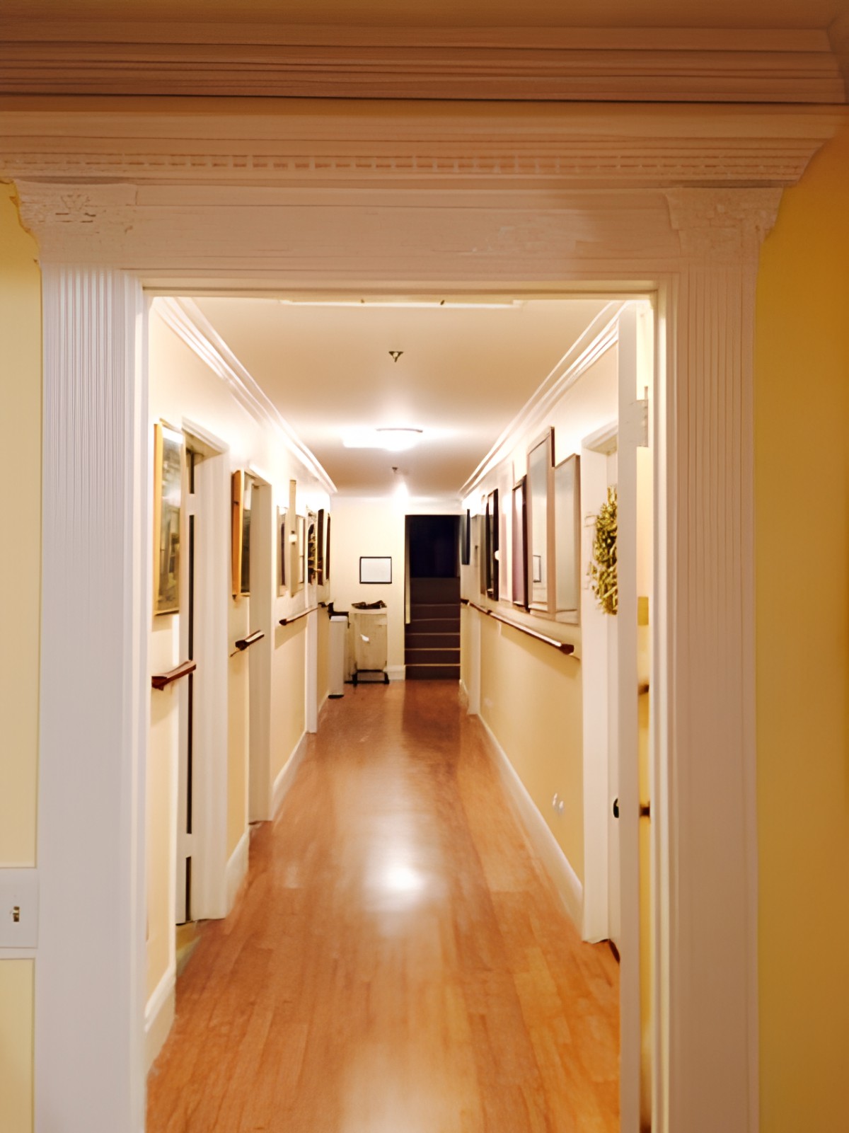 A well-lit hallway with wooden floors and paintings displayed on the walls.