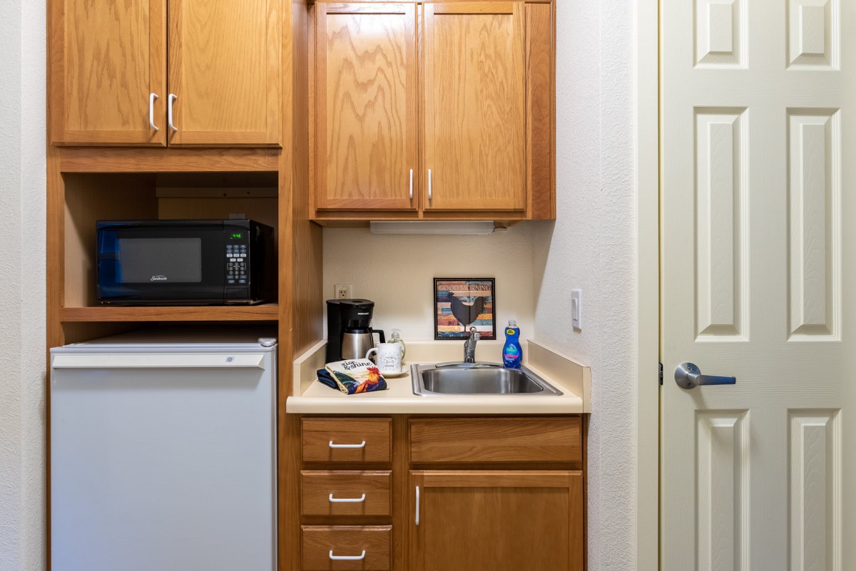 A compact kitchenette with wooden cabinets, a microwave, mini fridge, and sink.