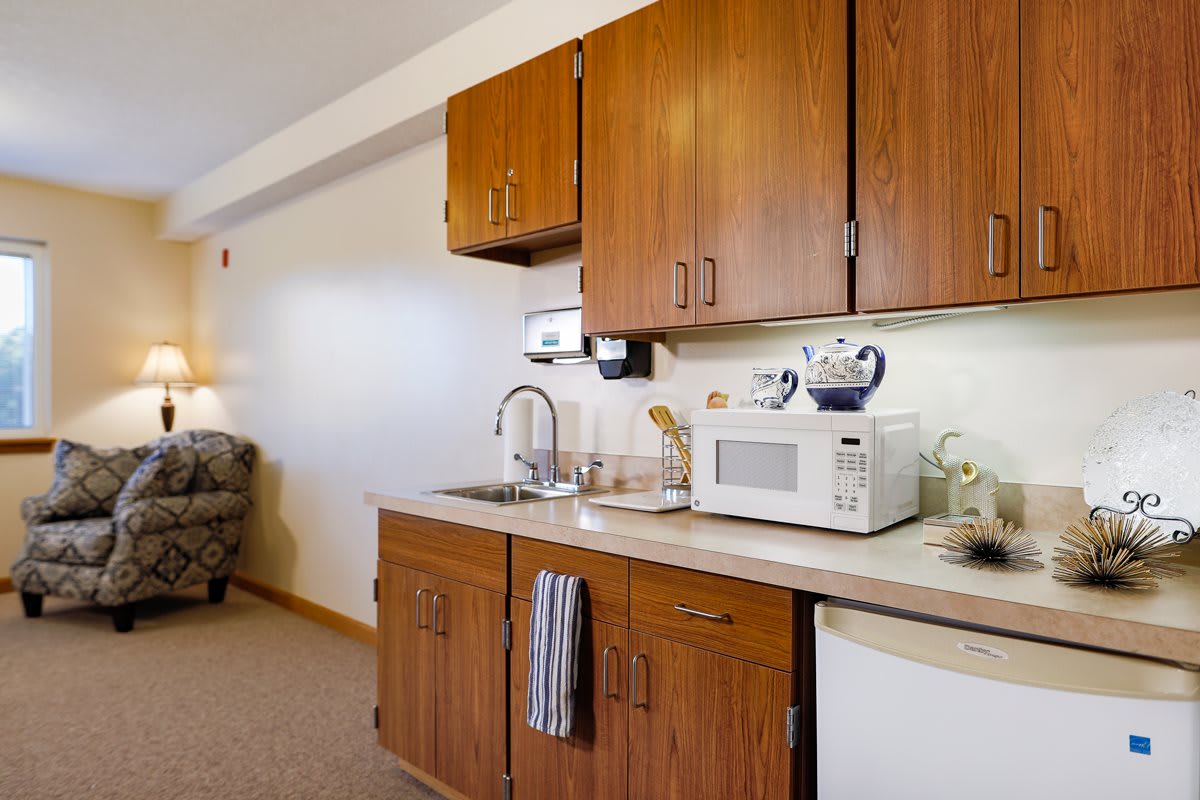 A compact kitchenette with wooden cabinets, featuring a microwave, sink, and countertop.