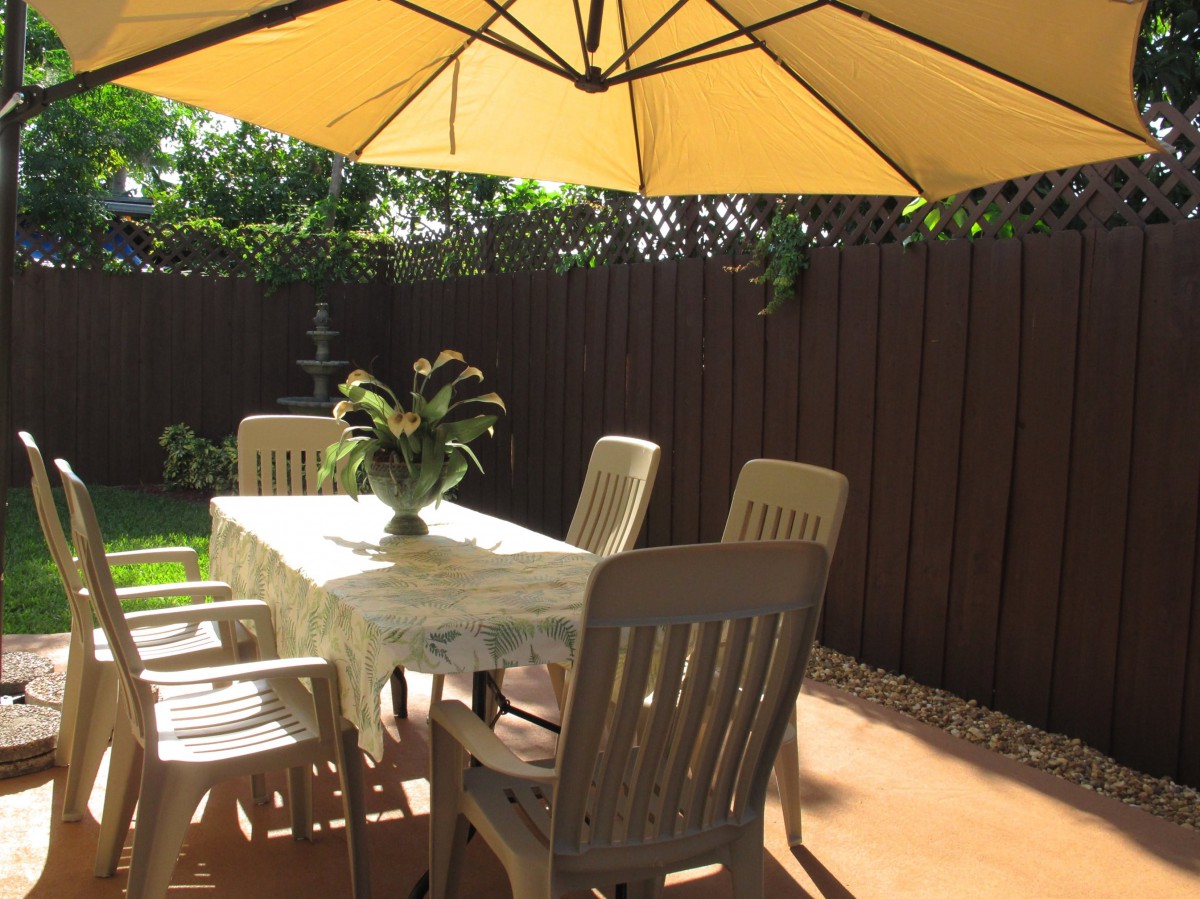 A sunny outdoor patio with a table, chairs, and a large umbrella.