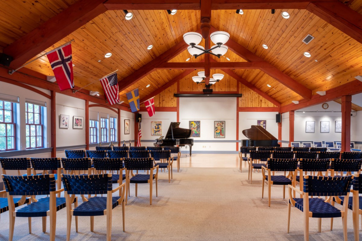 A concert hall with wooden ceilings, featuring two pianos on stage and flags hanging from the walls.