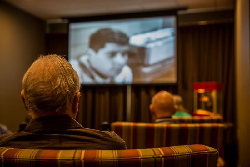Audience watching a black and white film in a theater setting.