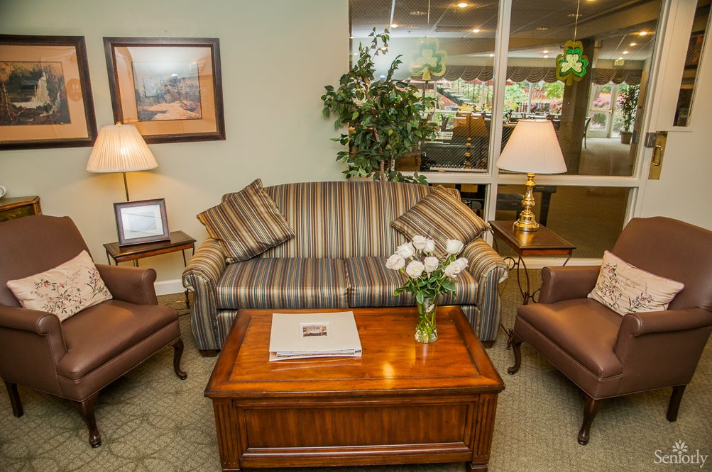 A cozy living room with a striped sofa, armchairs, and a wooden coffee table adorned with a vase of flowers, surrounded by warm lighting and decorative elements.