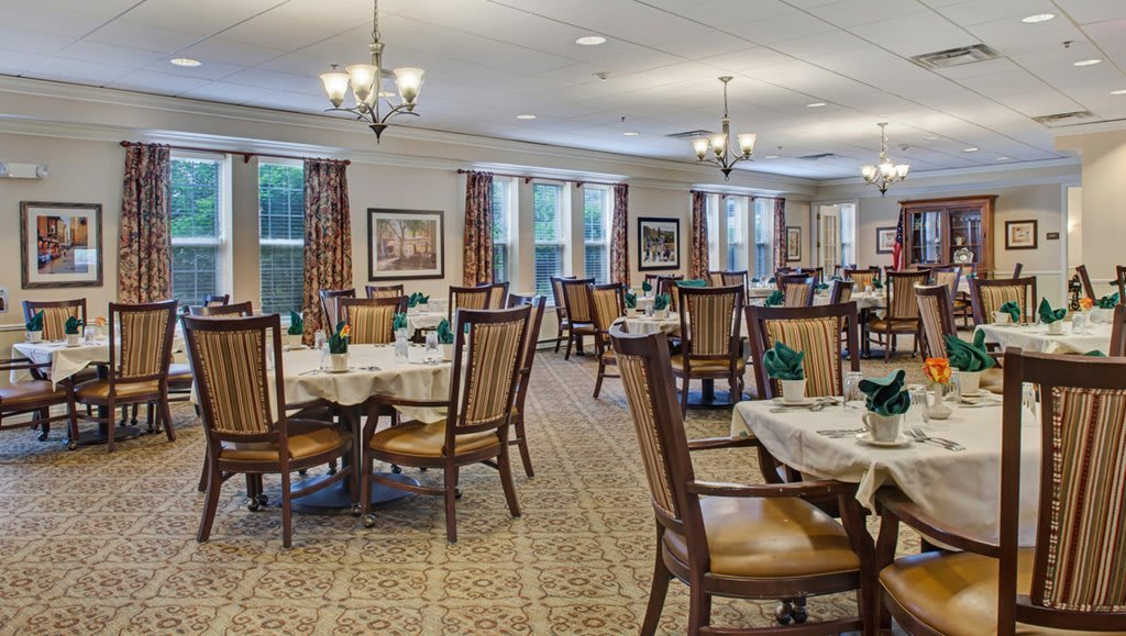An elegant dining room with neatly arranged tables and chairs, featuring chandeliers and large windows.