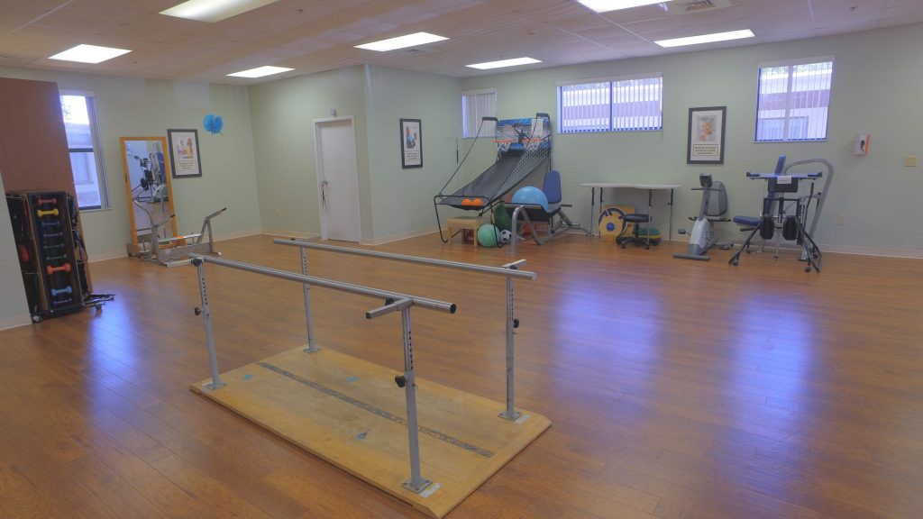 A rehabilitation therapy room equipped with parallel bars and various exercise equipment.