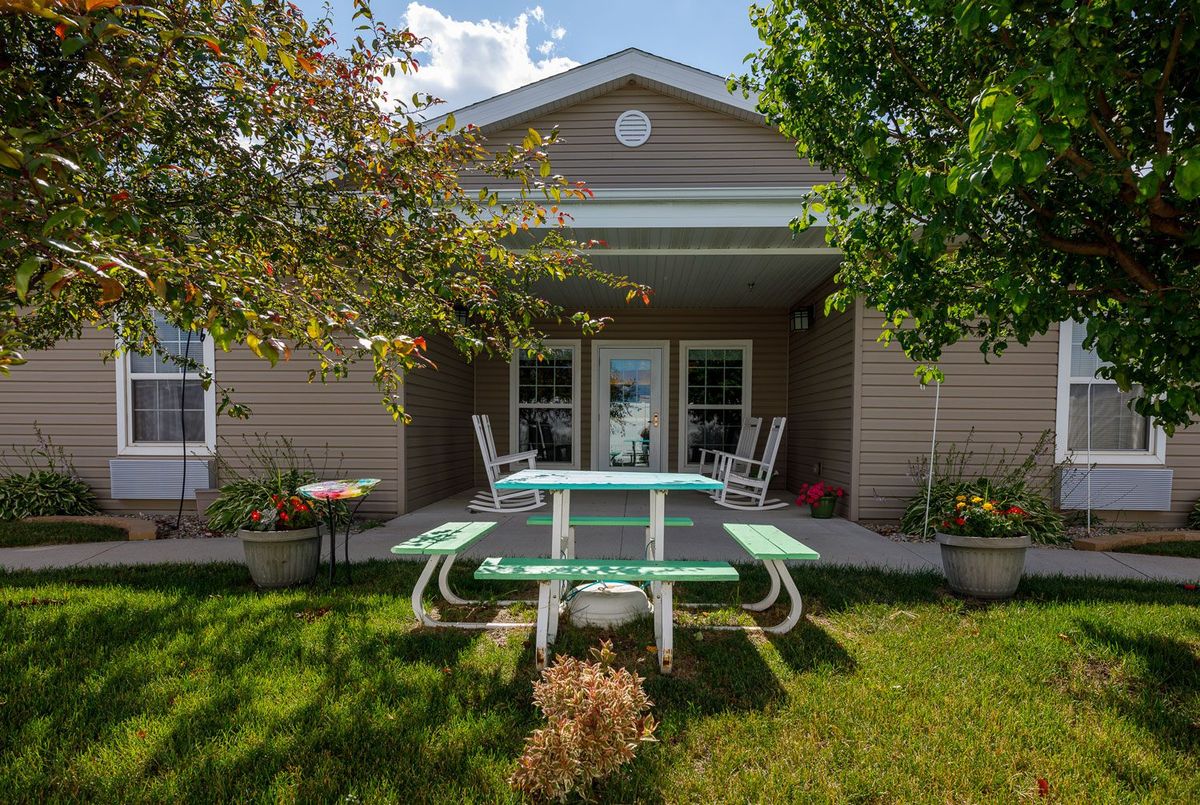 A cozy backyard with a picnic table, patio chairs, and surrounding greenery in front of a house.
