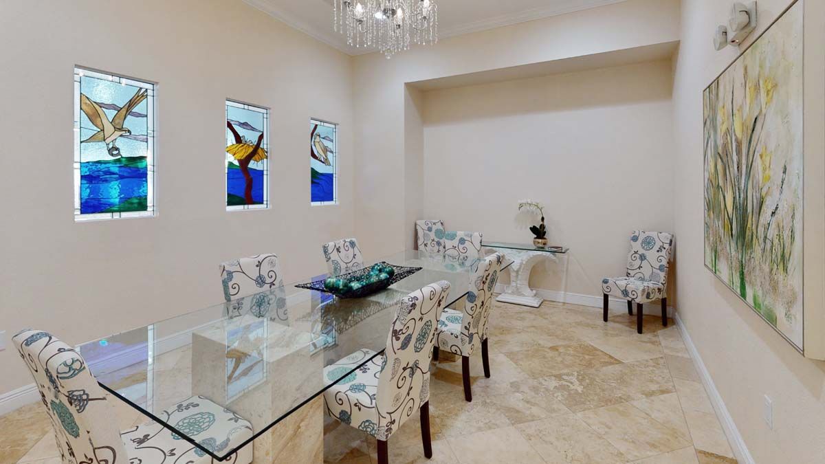 A modern dining room with a glass table and decorative chairs, highlighted by stained glass windows and a chandelier.
