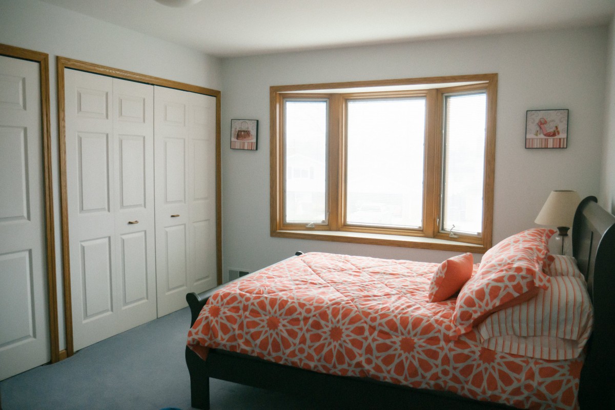 A cozy bedroom with a large window, featuring a bed with floral bedding and a spacious closet.