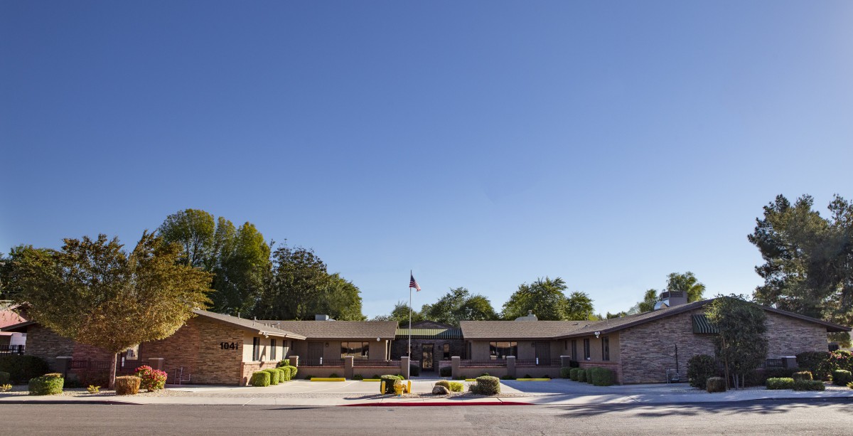 A residential building with a flagpole and trees under a clear blue sky.