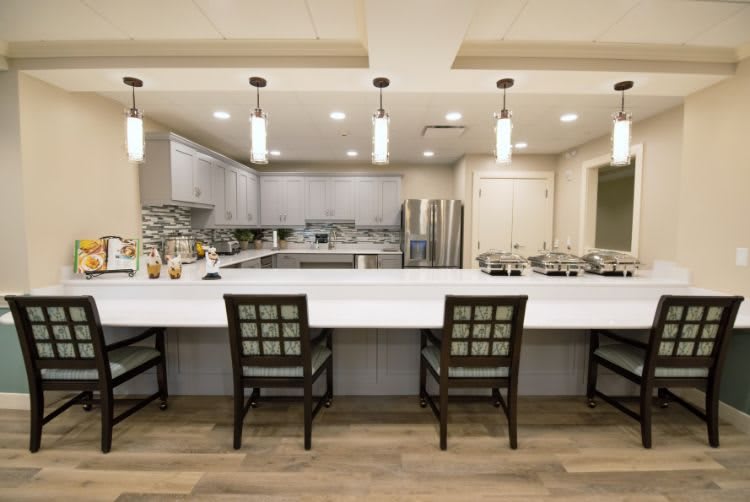 A modern kitchen with a large white countertop, bar stools, pendant lighting, and stainless steel appliances.