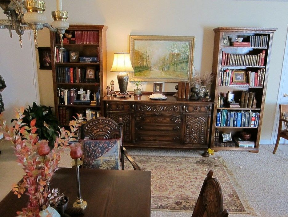 A cozy living room with bookshelves, a lamp, artwork, and a rug.