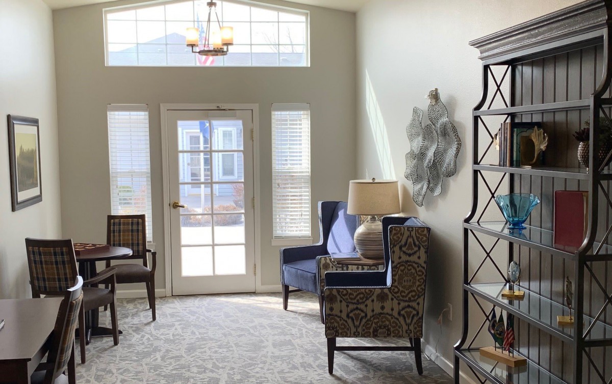 A bright living room featuring elegant chairs, a lamp, and large windows allowing natural light to fill the space.