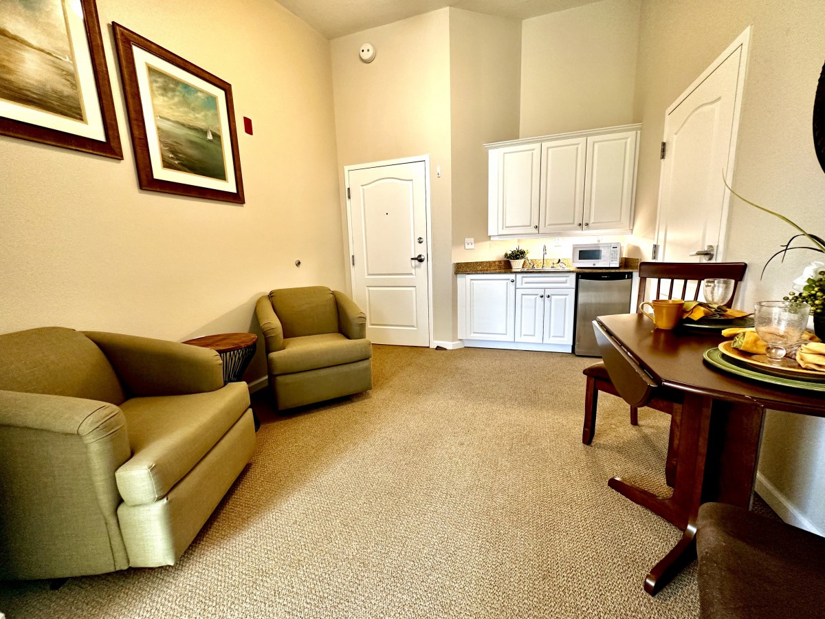A cozy living room with a kitchenette, featuring comfortable seating and tasteful artwork.