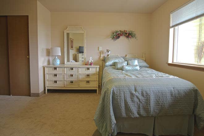 A cozy bedroom featuring a neatly made bed and a dresser with a mirror.