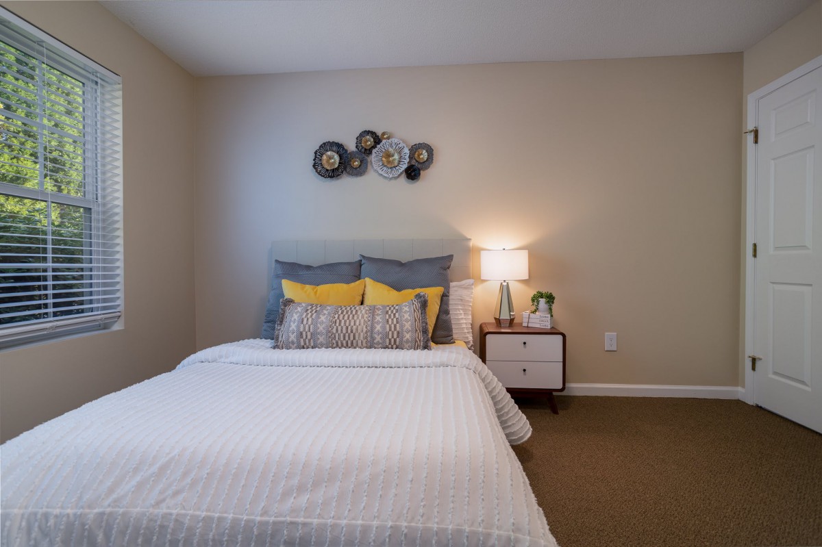A modern and cozy bedroom with a neatly made bed, decorative pillows, and a bedside table with a lamp.
