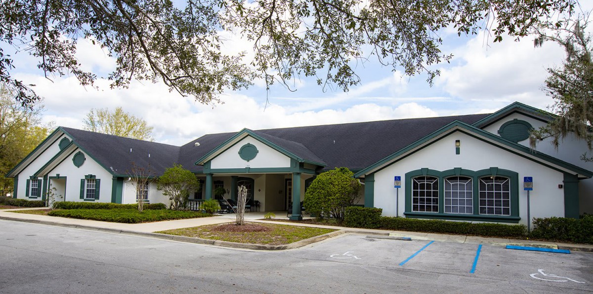 A single-story building with a front entrance and surrounding trees, viewed from a parking lot.