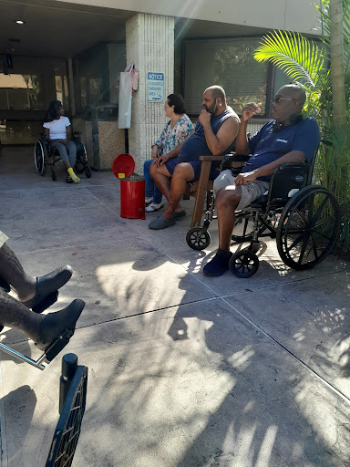 A group of individuals sitting outside a care facility, some in wheelchairs, enjoying the sunlight.