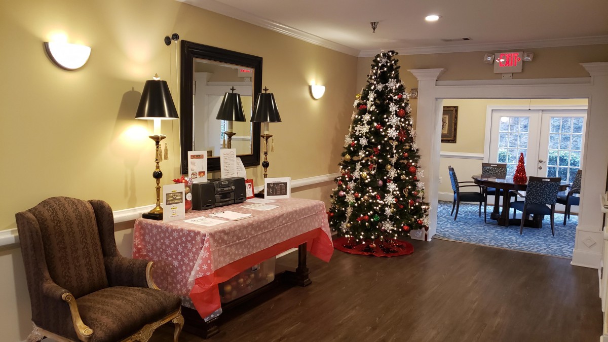A festive room with a decorated Christmas tree and a table covered in a red cloth, adorned with holiday decorations and two lamps.