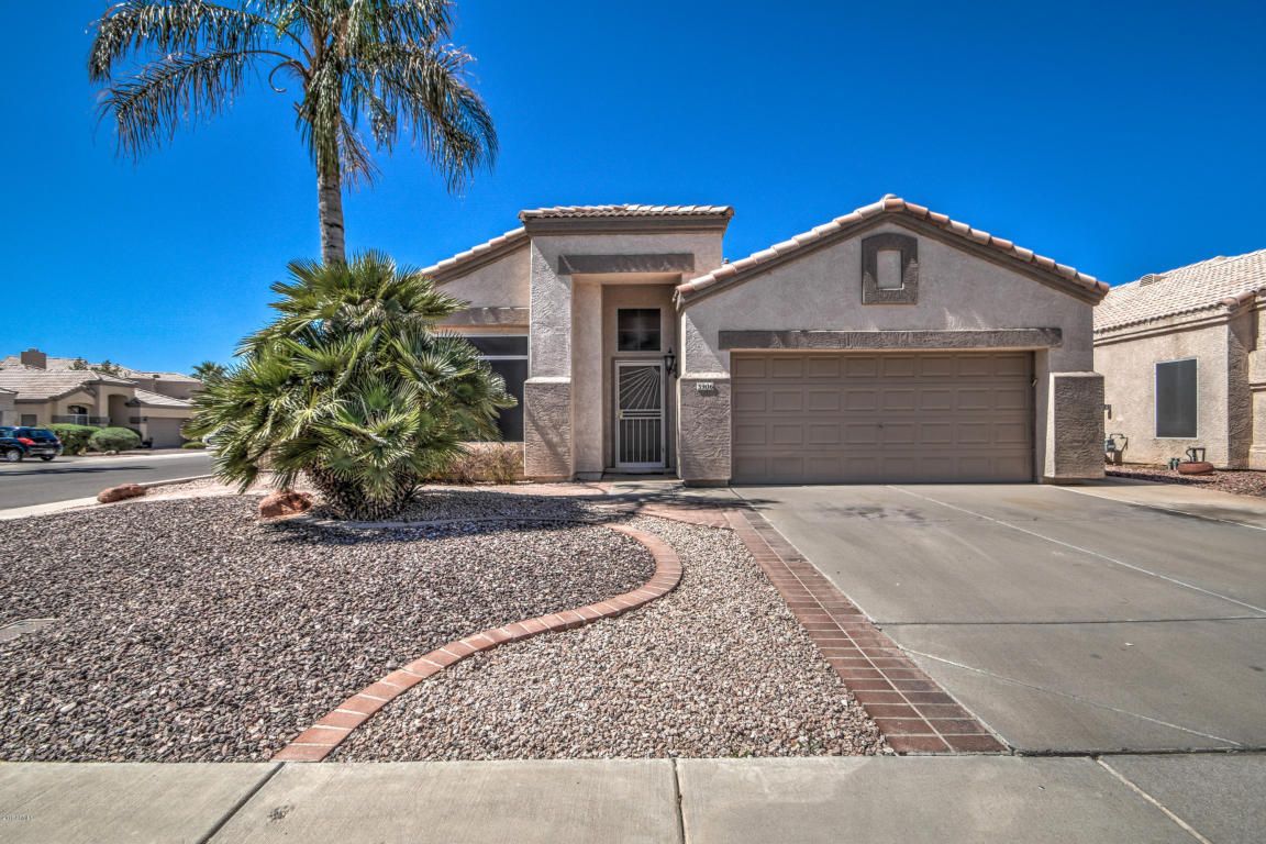 A suburban house with a dry landscape and palm tree, featuring a two-car garage and a clear blue sky.