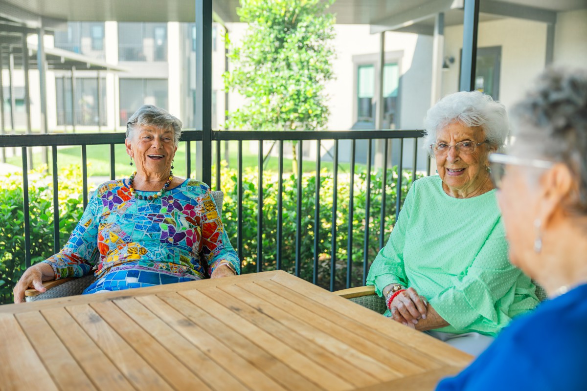 Two elderly women enjoying a sunny day outdoors while sitting at a wooden table.