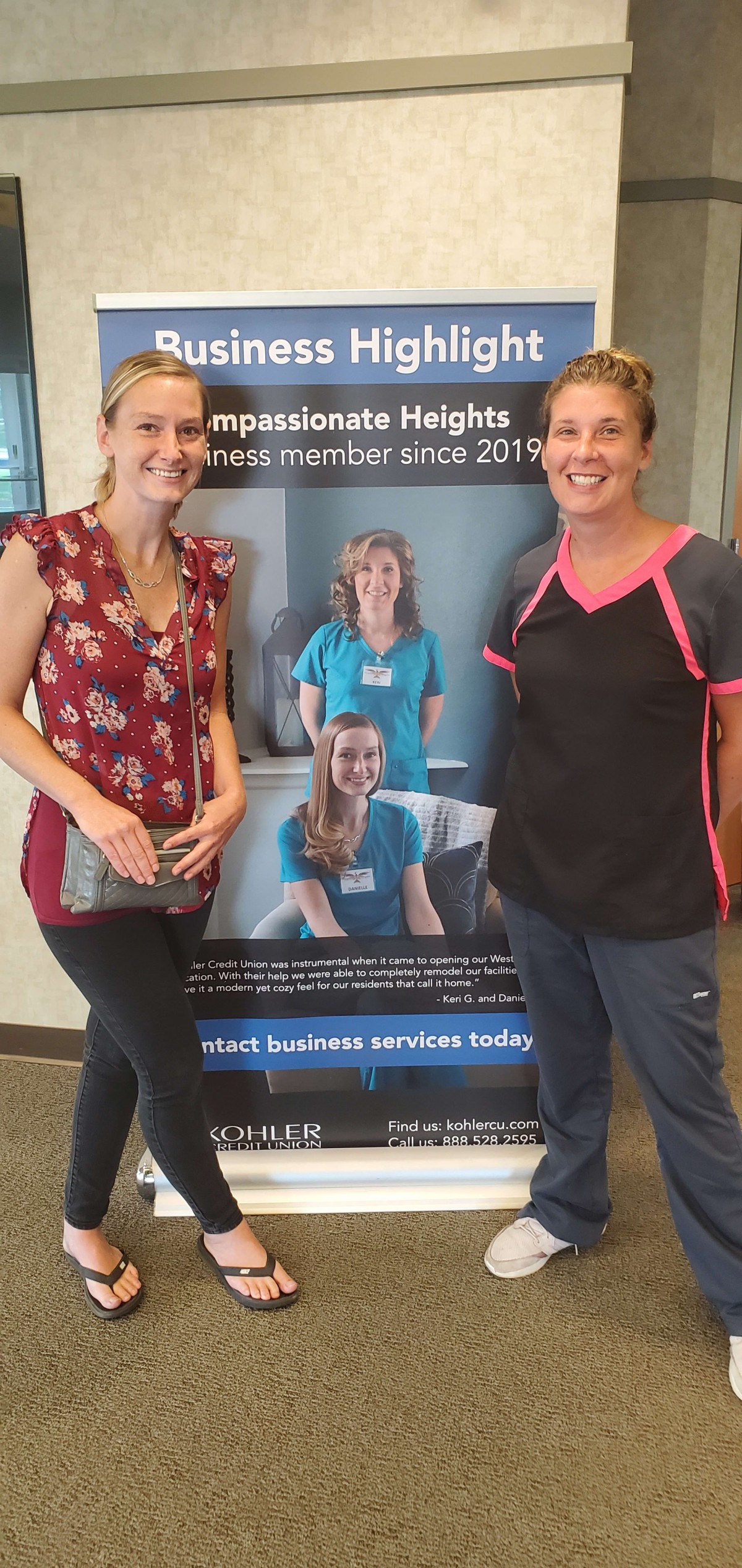 Two women standing next to a healthcare clinic poster.